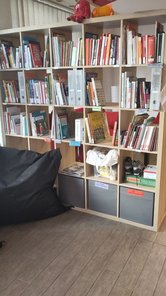 Ein großes quadratisches Regal, gefüllt mit Büchern. Davor liegt ein Sitzsack.