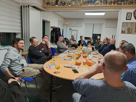 Im Vereinsraum der Feuerwehr in Wülfershausen ist eine lange Tafel aufgebaut. Daran sitzen circa 20 Menschen und diskutieren mit Christian Schaft über lokale Probleme.