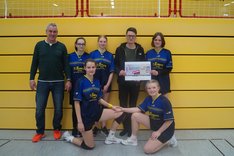 Christian Schaft übergibt einen Scheck an die Volleyball-AG. Zu sehen sind mehrere Mädchen in Trikots, sowie ein Trainer.
